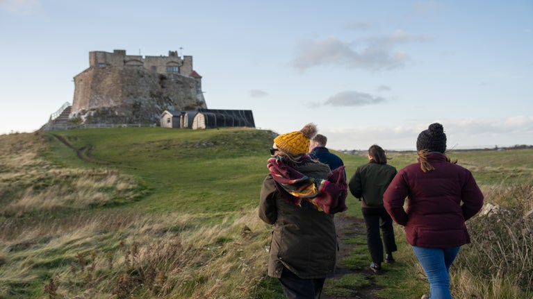 Group of people walking towards Lindisfarne Castle in the distance.